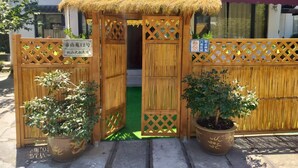 A wooden gate with a thatched roof entrance, a sign indicating a private residence, and two potted plants on either side.