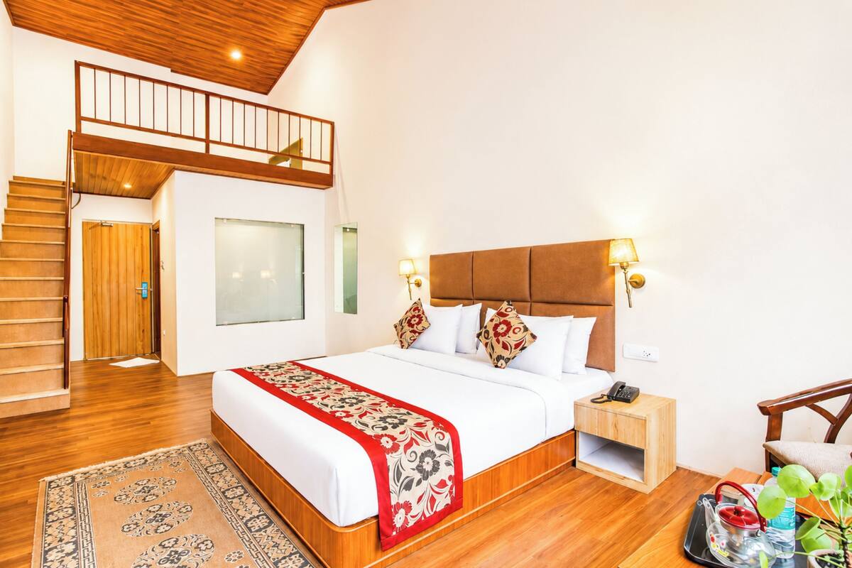 Un dormitorio con una cama grande, cabecera de madera, mesita de noche, escritorio, silla, escalera y vista al exterior.