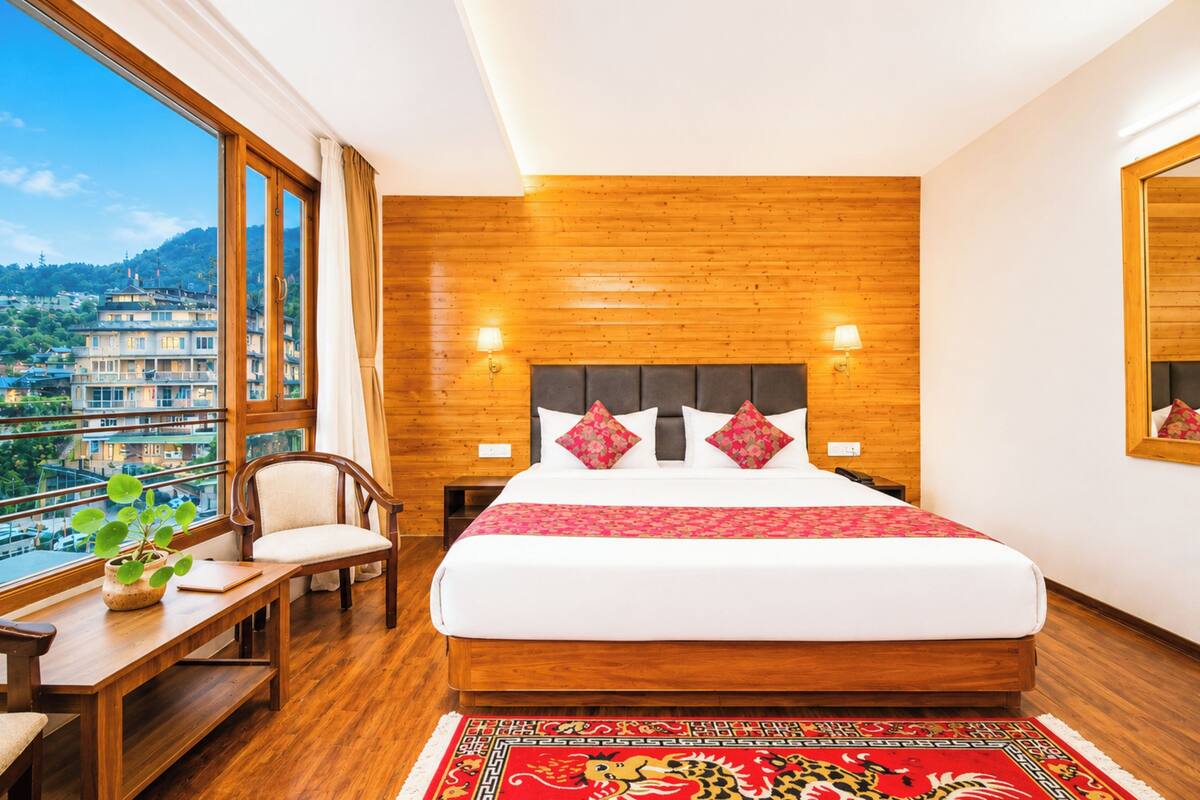 Habitación de hotel con una cama grande, paredes de madera, un escritorio con silla y vistas a un paisaje urbano.