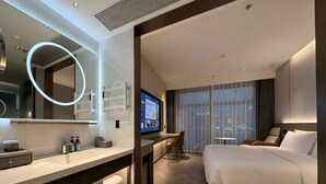 A modern hotel room with a large bed, a desk with a TV, a bathroom with a mirror and toiletries, and a city view through the window. - PALACE Hotel（Hangzhou Huayin Tower Hangzhou City University） (Hangzhou)