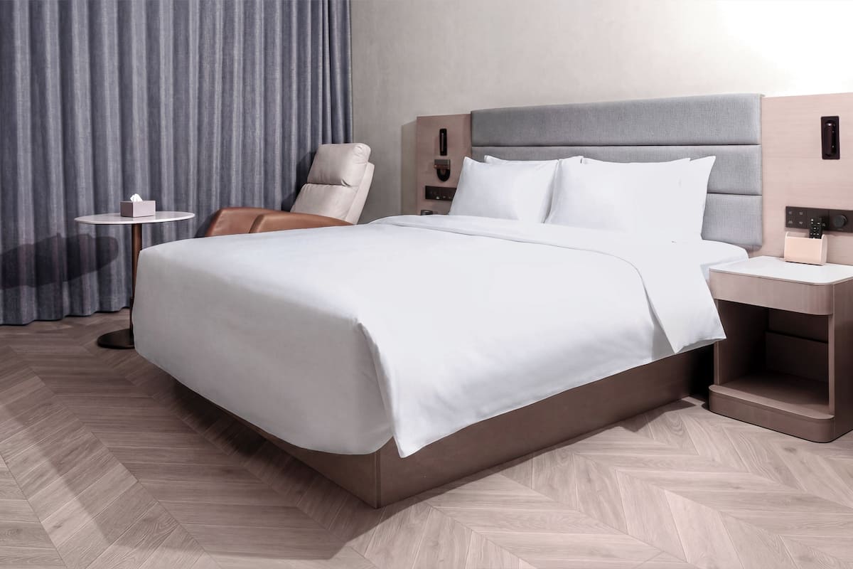 A modern hotel room with a large bed, a bedside table, a chair, and a curtain.