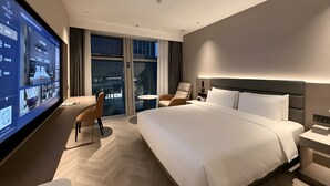 A modern hotel room with a large bed, a desk, a chair, a TV, and a view of the city through large windows. - PALACE Hotel（Hangzhou Huayin Tower Hangzhou City University） (Hangzhou)