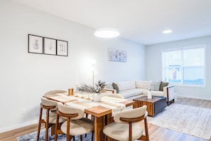 Una sala de estar moderna con comedor, un sofá, una mesa de centro y un ventanal con persianas.