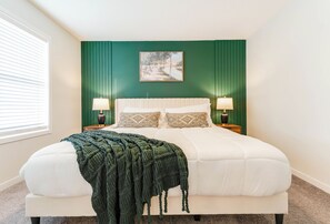 Un dormitorio con una cama, dos mesitas de noche, un ventanal con persianas y una pared verde.