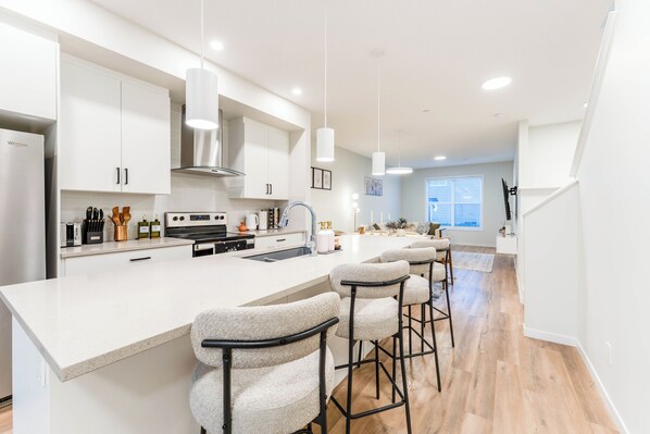 Una cocina moderna con armarios blancos, una isla central con taburetes y un amplio ventanal que proporciona luz natural.