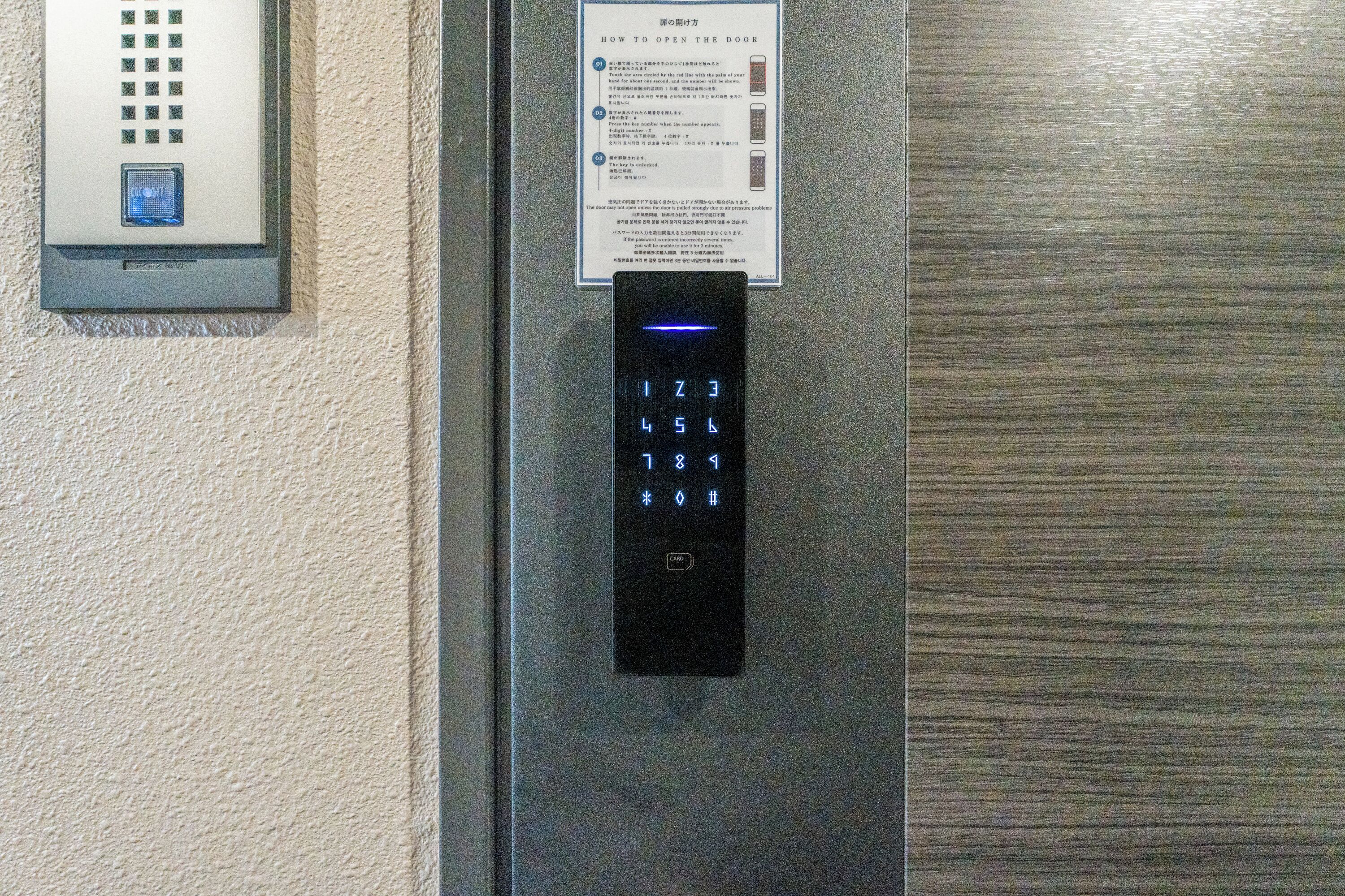 A digital keypad lock on a door, a wall-mounted intercom, and a sign with instructions.