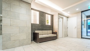 A modern lobby with a stone wall, a wicker sofa, and a glass door leading outside. - Eslead Hotel Namba East Annex (Oosaka)