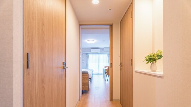A hallway with wooden doors, a white wall, and a plant on a shelf. - Eslead Hotel Namba East Annex (Oosaka)