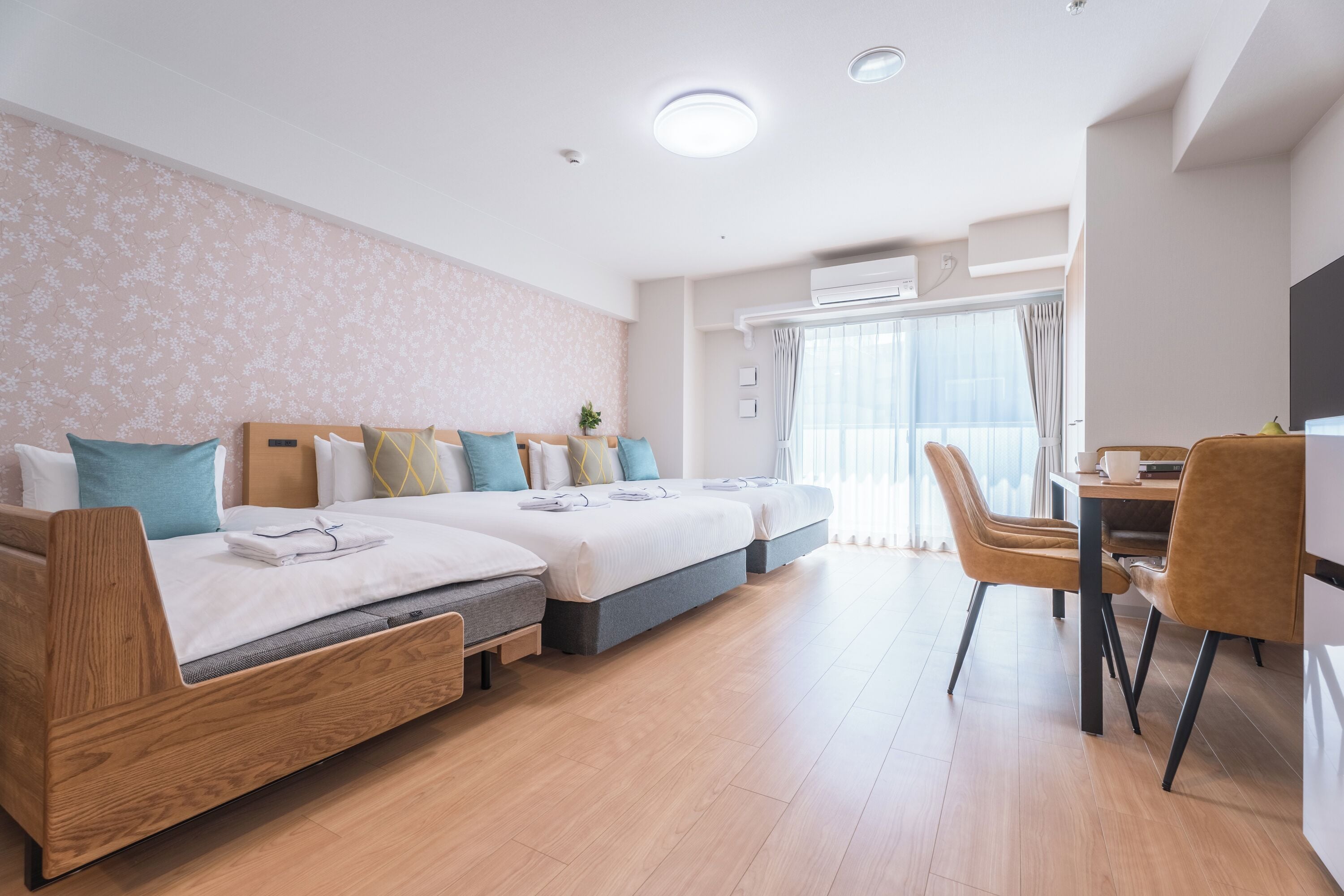 A modern hotel room with two beds, a dining area, and a large window.