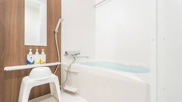 Un baño con una bañera blanca, un taburete blanco, un espejo y un estante con artículos de aseo.