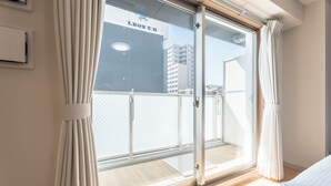 A room with a large sliding glass door leading to a balcony, a bed, and a visible building with 'LEON U.D.' on it. - Eslead Hotel Namba East Annex (Oosaka)
