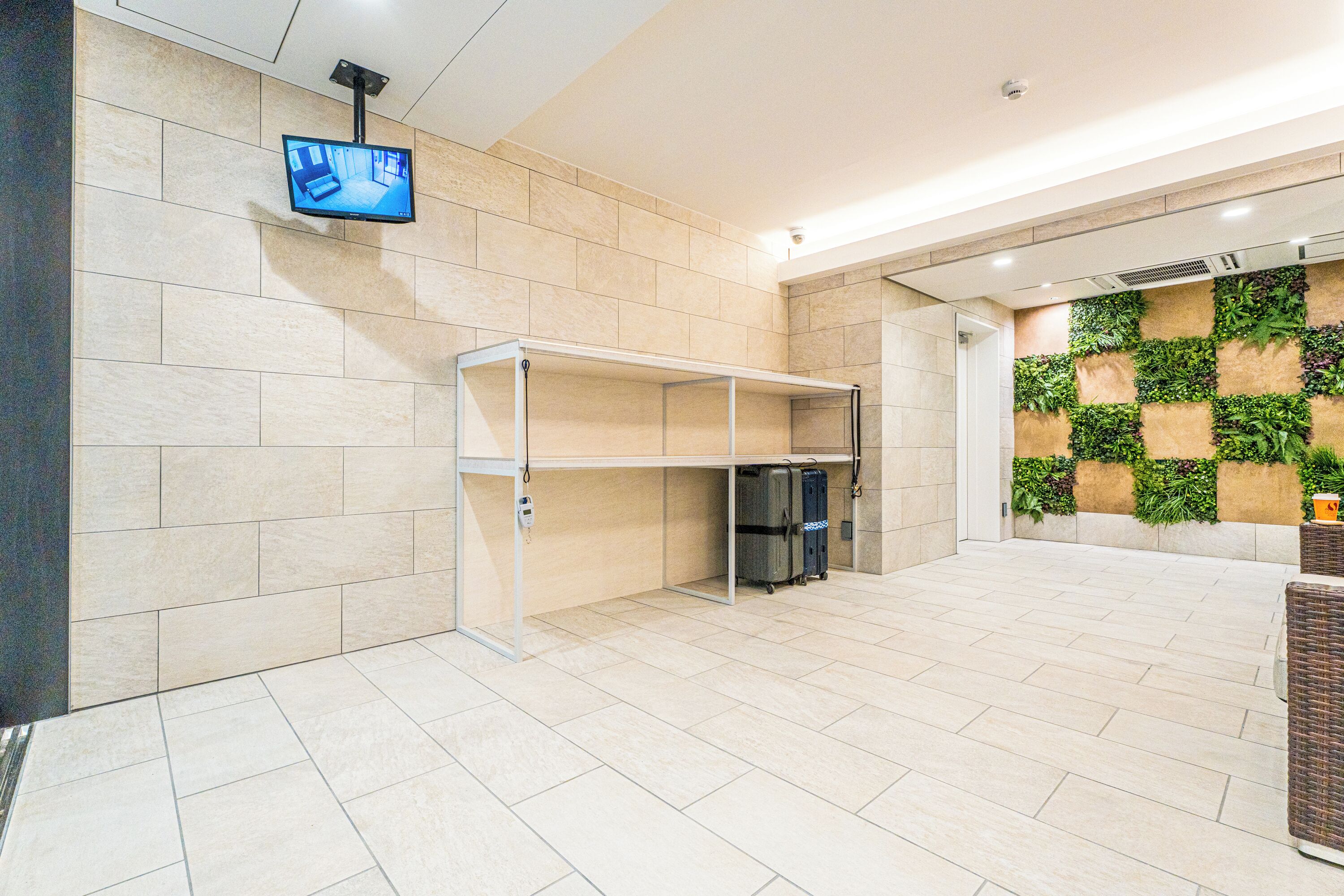 Een hotel lobby met een betegelde vloer, een wandtelevisie, een glazen vitrine en een wand bedekt met groen.'