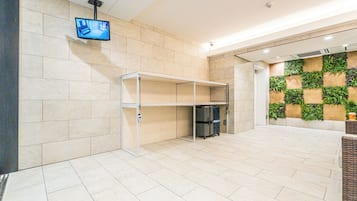 A hotel lobby with a tiled floor, a mounted television, a glass display case, and a wall with a green plant wall.