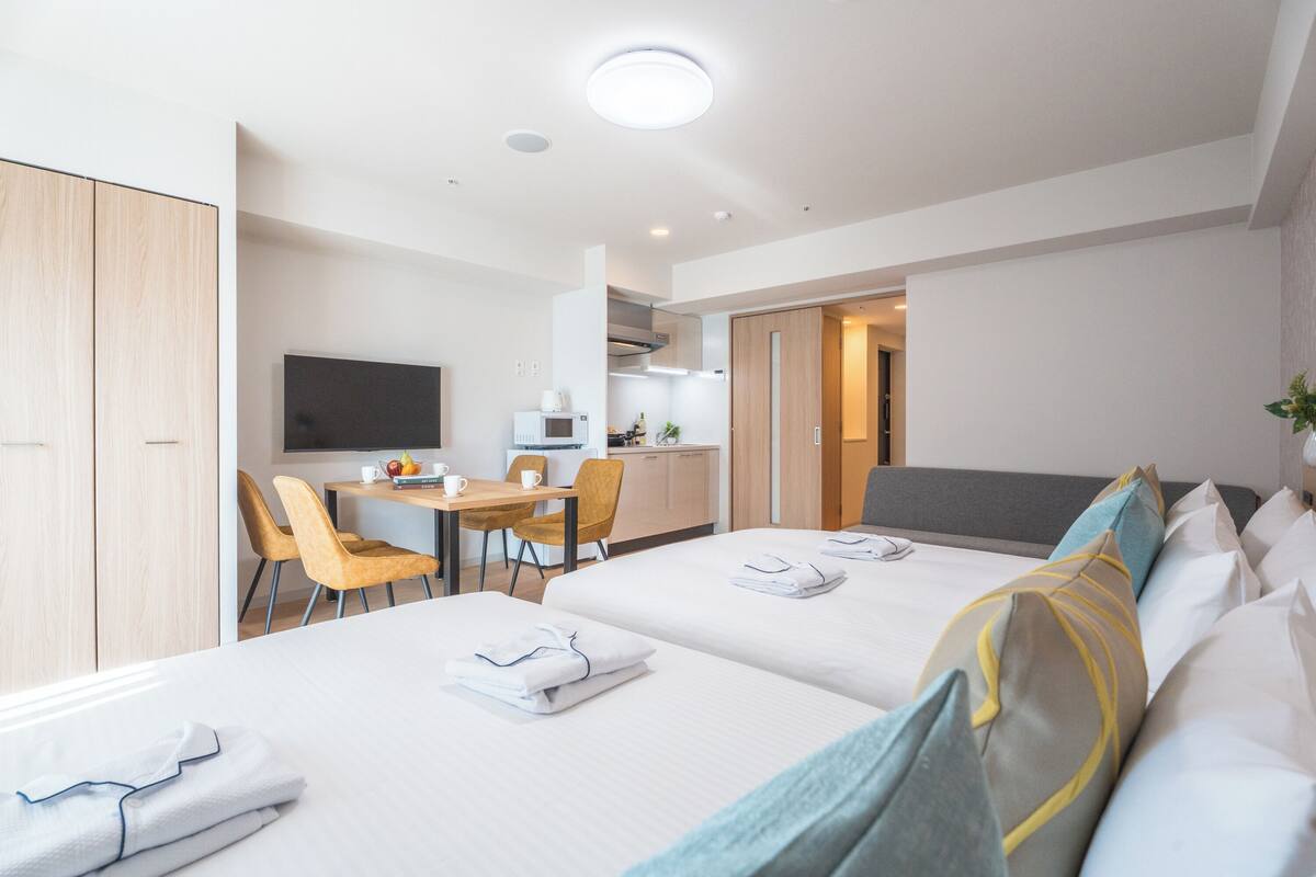 Habitación de hotel con dos camas, un escritorio, televisión y kitchenette.
