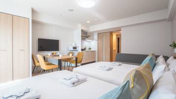 A hotel room with two beds, a desk, a TV, and a kitchenette.