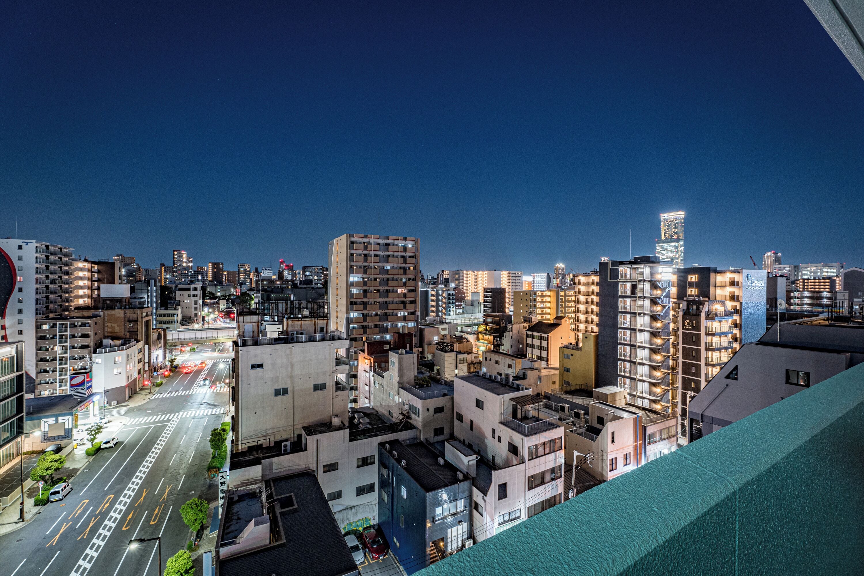 A cityscape at night with high-rise buildings, a clear sky, and a view of the street below.