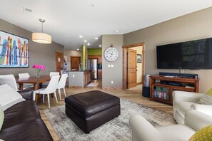 A modern living room with a dining area, kitchen, and a TV mounted on the wall. - Purgatory Alpine Retreat | Walk to Lifts & Base Area | Pool/Hot Tub (Durango)