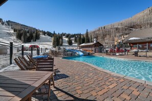 A pool area with lounge chairs, a water slide, and a view of a ski slope. - Purgatory Alpine Retreat | Walk to Lifts & Base Area | Pool/Hot Tub (Durango)