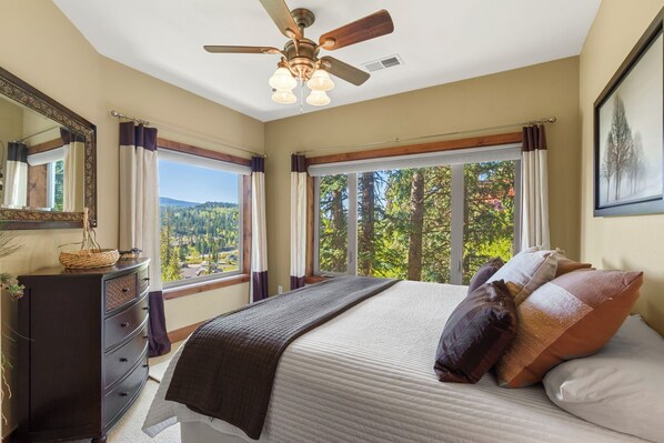 A bedroom with a bed, a dresser, a ceiling fan, and a window with a view of trees. - Purgatory Alpine Retreat | Walk to Lifts & Base Area | Pool/Hot Tub (Durango)