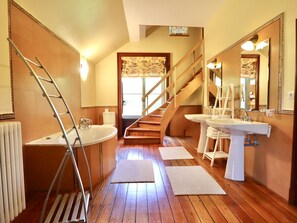 A bathroom with a wooden floor, two sinks, a bathtub, a staircase, and a radiator.
