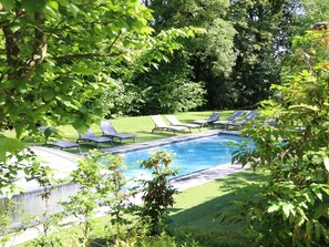 A swimming pool surrounded by green grass and trees, with several lounge chairs.