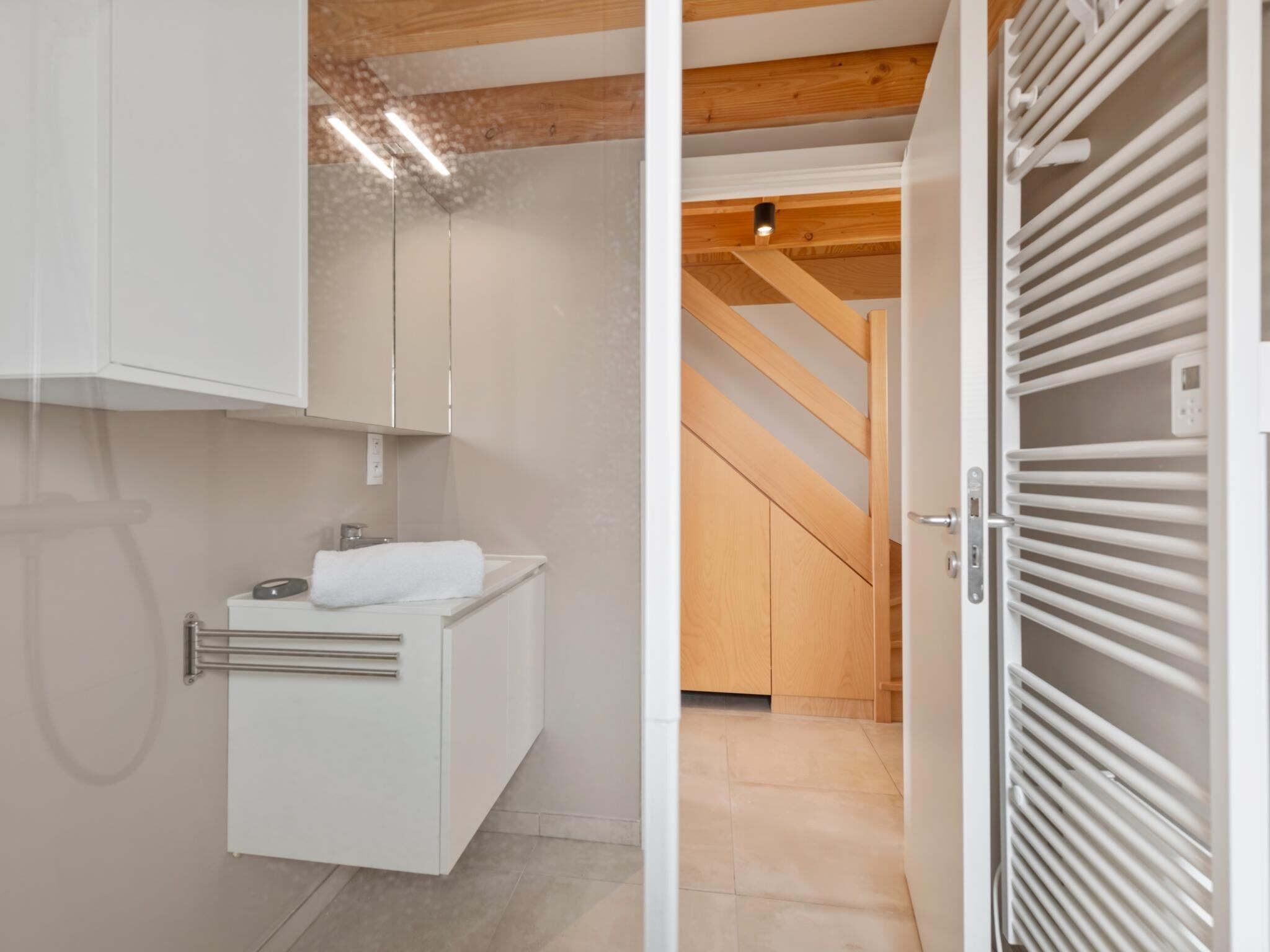 Een moderne badkamer met een wit aanrecht, een handdoek en een houten trap op de achtergrond.