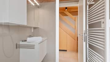 Een moderne badkamer met een wit aanrecht, een handdoek en een houten trap op de achtergrond.