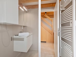 A modern bathroom with a white vanity, a towel, and a wooden staircase in the background.