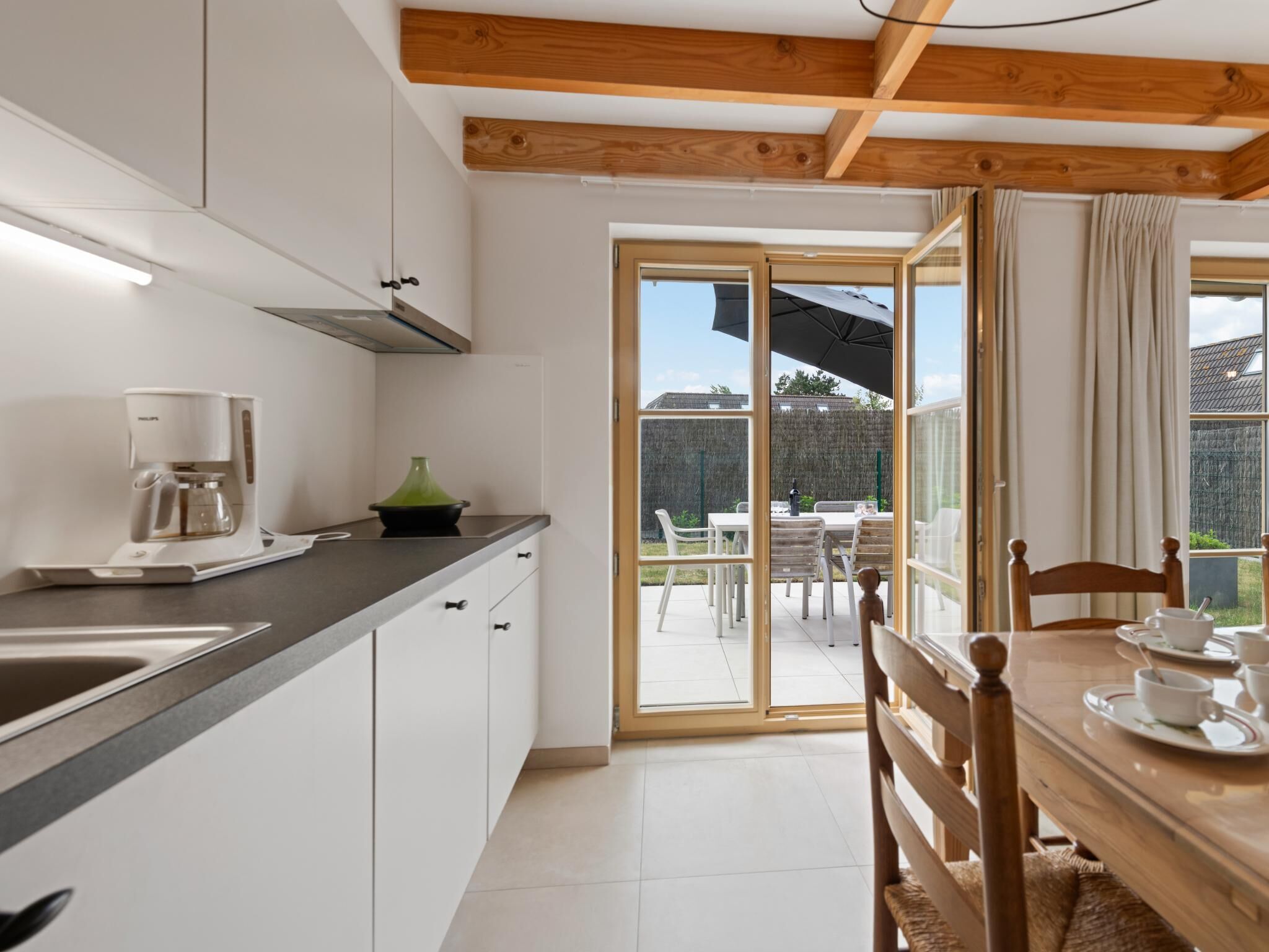 Een moderne keuken met witte kastjes, een koffiezetapparaat en een eethoek met een tafel en stoelen.