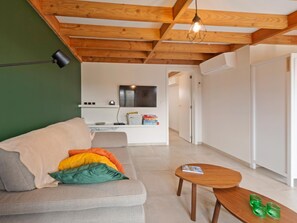 Ein Wohnzimmer mit einer Couch, einem Couchtisch, einem Fernseher und einer Küche im Hintergrund.