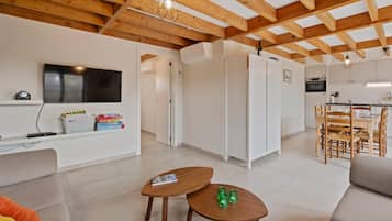 Een moderne woonkamer met een houten plafond, een aan de muur bevestigde televisie, een bank, een salontafel en een eethoek met stoelen.