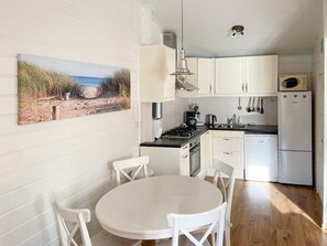 Eine Küche mit weißen Schränken, einem Herd, einer Mikrowelle und einem Kühlschrank. An der Wand hängt ein Gemälde mit einer Strandansicht.
