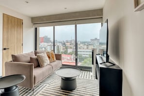 Ein modernes Wohnzimmer mit Sofa, Couchtisch und Fernseher, große Fenster mit Blick auf die Stadt.