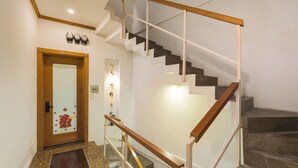 Una escalera con barandilla de madera y balaustradas de vidrio, que conduce a un rellano con una puerta decorada con motivos florales.