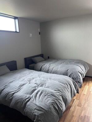 Une chambre avec deux lits, un plancher en bois et une fenêtre.