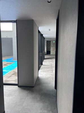 Un couloir avec une porte en verre donnant sur un espace carrelé de carreaux bleus, un mur en pierre et une porte sur laquelle figure un panneau vert indiquant la sortie.