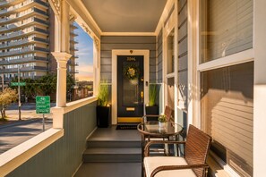 Entrada de hotel com porta preta marcada '3046', mesa de vidro com cadeiras e vista de um edifício alto.