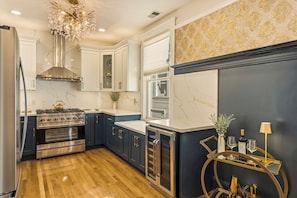 Cozinha moderna com eletrodomésticos de aço inoxidável, bancadas de mármore e um lustre decorativo.