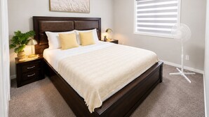 A neatly made bed with a dark headboard, a bedside lamp, and a floor fan. - Stay Cool! -Modern 3BR Home Near YYC with New Central AC (Calgary)