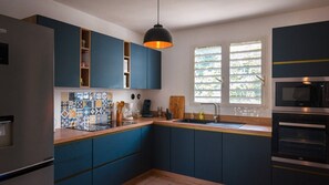 Eine moderne Küche mit blauen Schränken, einer gefliesten Spritzschutzwand, einem Einbauofen und einem Fenster mit Jalousien.