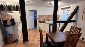 Une cuisine équipée d’une table et de chaises, d’une machine à café et d’une fenêtre avec des stores.