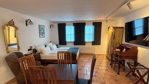 Une pièce comprenant un lit, une table à manger avec des chaises, un piano, une télévision et un grand miroir.