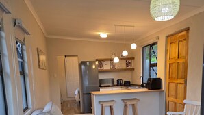 A modern kitchen with a central island, wooden stools, and pendant lighting. - Tranquil 1-bedroom Apartment Near Gonubie Beach (East London)