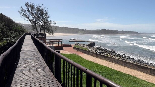 A wooden boardwalk leading to a beach with a rocky shoreline and waves. - Tranquil 1-bedroom Apartment Near Gonubie Beach (East London)
