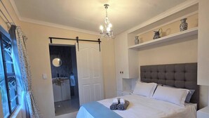 A bedroom with a bed, a chandelier, a window with curtains, and a wooden floor. - Tranquil 1-bedroom Apartment Near Gonubie Beach (East London)