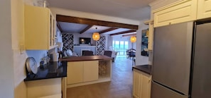 A kitchen with a central island, wooden beams, a refrigerator, and a dining area with a view.