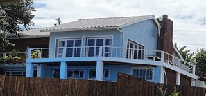 Una casa de dos pisos con balcón, chimenea de ladrillo y cerca de madera.