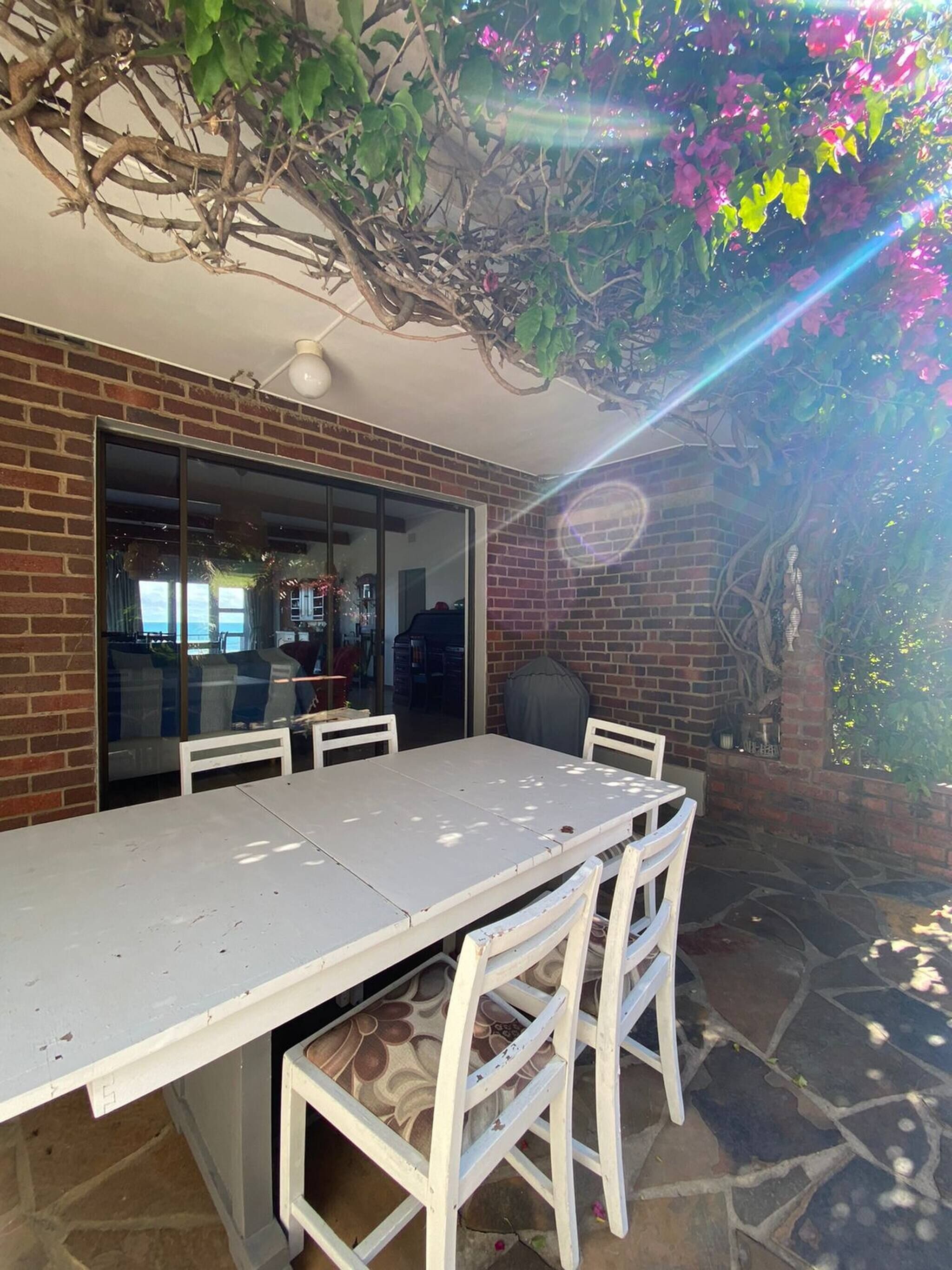 Une terrasse avec une table et des chaises, un mur en briques et une porte vitrée donnant sur un espace intérieur.