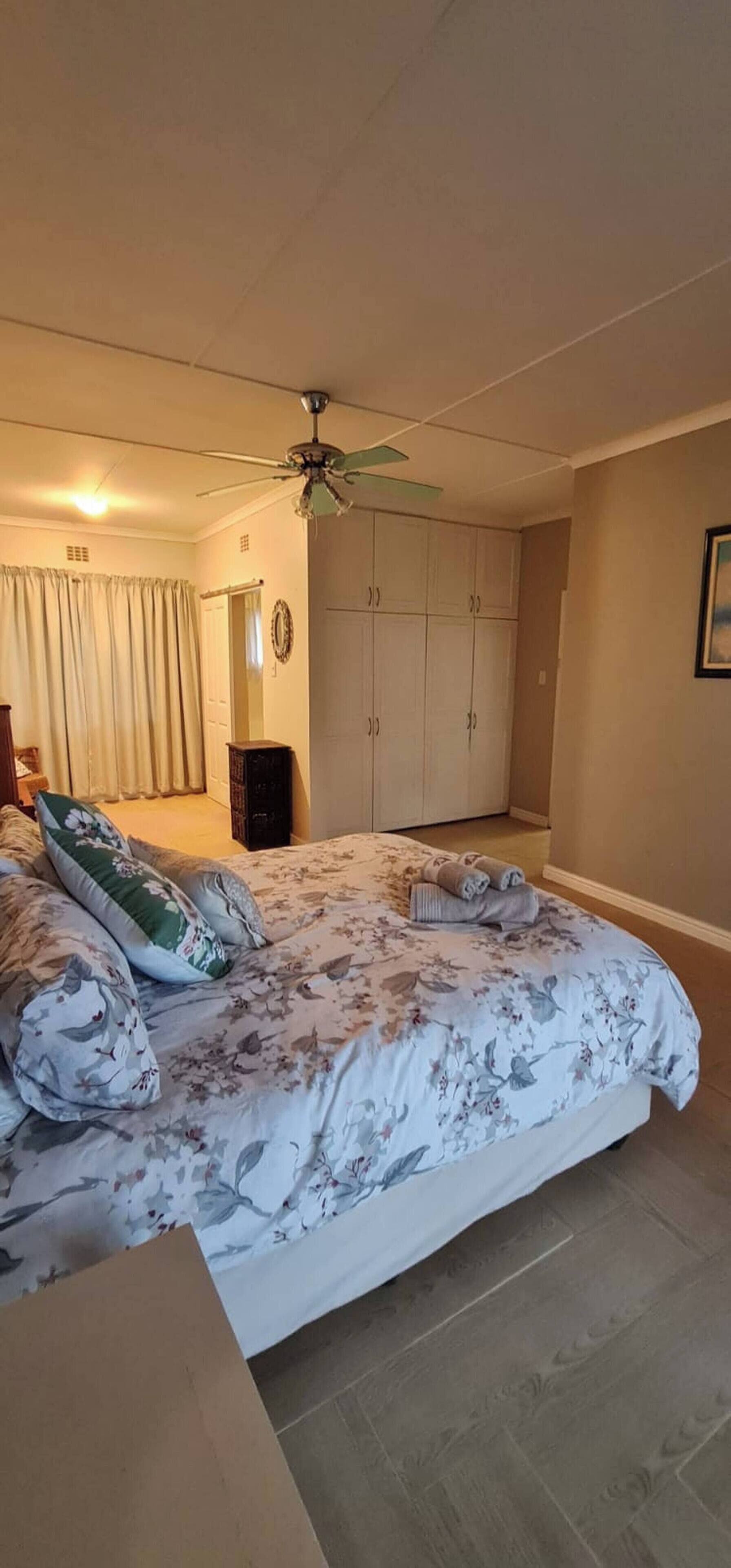 Une chambre à coucher comprenant un lit, un ventilateur de plafond, une armoire et une porte donnant sur une autre pièce.