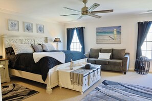Une chambre à coucher comprenant un lit, un canapé, une table de chevet, un ventilateur de plafond et des œuvres d’art accrochées aux murs.